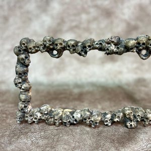 May include: A silver metal license plate frame decorated with a border of small skull shapes.