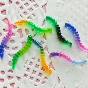 May include: Assortment of colorful, flexible, worm-shaped plastic charms. The charms are in shades of green, blue, pink, and yellow.