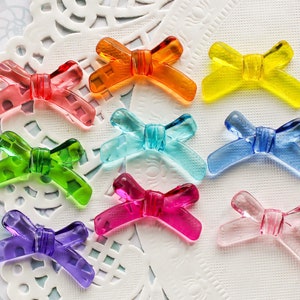 May include: Assortment of ten colorful plastic bow-shaped charms in various colors, including pink, green, blue, yellow, and orange.