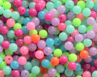May include: A large pile of colorful plastic beads in shades of pink, purple, blue, green, and orange. The beads are all round and have a glossy finish.
