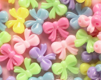May include: A collection of pastel-colored plastic bow-shaped beads. The beads are in shades of pink, purple, blue, green, and yellow.
