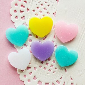 May include: Five heart-shaped resin embellishments in various colors, including yellow, pink, light blue, turquoise, and white. The hearts are on a white doily.