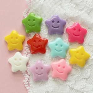 May include: Ten colorful star-shaped buttons with smiling faces. The buttons are arranged in a circle on a white lace background.