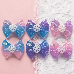 May include: Six resin bows with a snowflake design. The bows are in shades of blue, purple, and pink.
