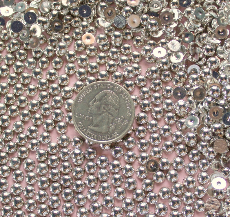 May include: A close-up image of a large quantity of silver-colored round beads. The beads are arranged in a random pattern and are all the same size. A US quarter is included in the image for scale.