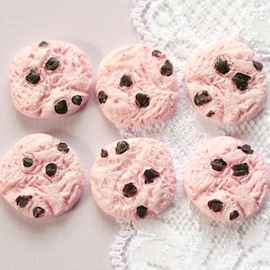 May include: Six pink and brown chocolate chip cookies. The cookies are round and have a textured surface. They are arranged in two rows of three.