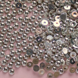 May include: A large pile of silver-colored round embellishments with a raised center. Some of the embellishments are flat and have a slightly raised center.