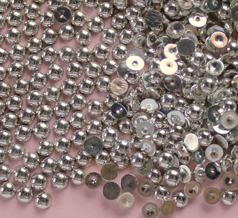 May include: A large pile of silver-colored round embellishments with a raised center. Some of the embellishments are flat and have a slightly raised center.