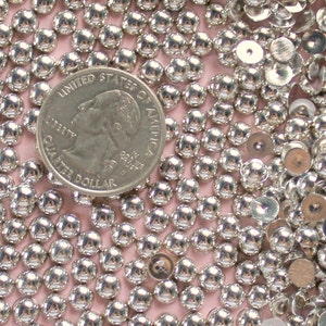 May include: A close-up image of a large quantity of silver-colored round beads and sequins. A US quarter is included for scale.