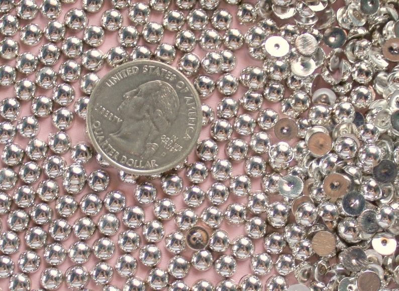 May include: A close-up image of a large quantity of silver-colored round beads and sequins. A US quarter is included for scale.