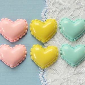 May include: Six heart-shaped resin embellishments in pink, yellow, and blue. Each heart has a scalloped edge.