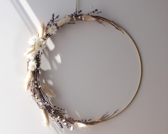 May include: A circular wreath with a gold metal frame, adorned with dried white flowers, lavender, and fluffy beige grasses. The wreath is suspended by a natural twine cord against a white wall. The word "LOT450" is visible in the lower left corner.