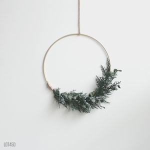 May include: A gold metal hoop wreath adorned with evergreen foliage and small blue-grey berries. The wreath is suspended by a natural twine cord against a white background. The text "LOT450" is in the lower left corner.