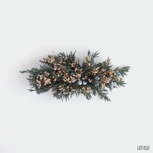May include: A green and brown floral arrangement with small blue berries. The arrangement is on a white background.
