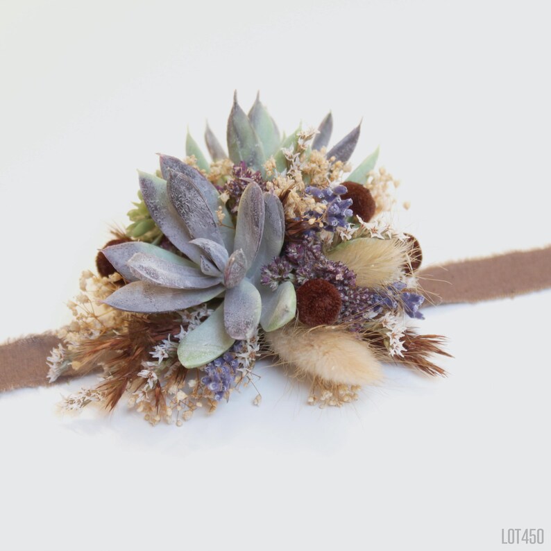 May include: A dried floral wrist corsage with a brown ribbon. The corsage features a variety of dried flowers, including succulents, lavender, and pampas grass.