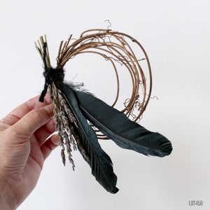 Puede incluir: Una corona hecha de ramitas marrones con plumas negras y ramitas de lavanda secas adjuntas.