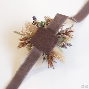 May include: A brown velvet ribbon tied around a dried flower bouquet with a brown felt backing. The bouquet includes dried grasses, lavender, and other dried flowers.