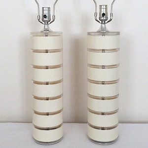 May include: Pair of cylindrical table lamps. Each lamp features a stacked design with alternating cream-colored and clear acrylic sections. The lamps have chrome bases and finials, and a silver lamp holder.