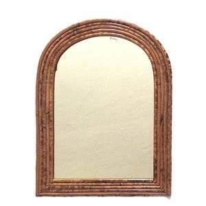 May include: An arched mirror with a natural, light brown bamboo frame. The frame is constructed of multiple layers of bamboo, creating a textured, layered effect. The mirror's glass surface reflects the surrounding environment.