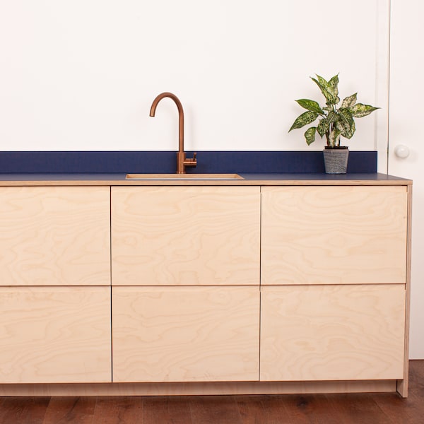 May include: A kitchen sink with a copper faucet and a blue countertop. The sink is set into a cabinet with six wooden doors.