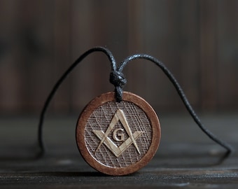 May include: A wooden pendant with a black cord, featuring a carved Masonic symbol with a 'G' in the center.