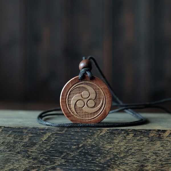 Collier/pendentif symbole Tomoe. Fabriqué à partir de bois de sycomore massif. Forme ronde. Couleur brune. Cordon de coton réglable. Personnalisation du texte.