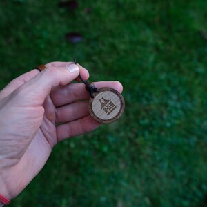 Puede incluir: Un llavero de madera con un cord&oacute;n negro. El llavero tiene una etiqueta redonda de madera con el texto "御利益" grabado en ella.