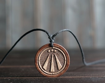 May include: A wooden pendant necklace with a brown and white symbol, the symbol is a circle with three lines and three dots inside.