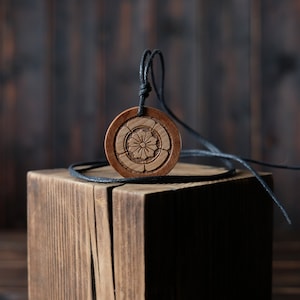 May include: A wooden pendant necklace with a carved floral design. The pendant is brown and the necklace is black.