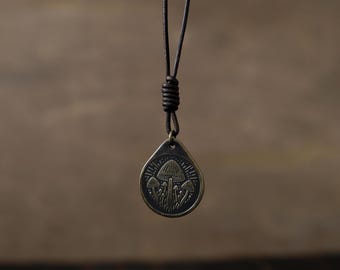 May include: A brown leather cord necklace with a bronze pendant featuring a detailed design of three mushrooms.