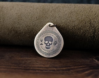 May include: A brass pendant with a skull, hourglass, and rose design. The pendant is engraved with the text "Memento Mori" and "Memento Vivere" in a Greek key border.