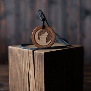 May include: A wooden pendant necklace with a wolf howling at the moon design. The pendant is brown and the cord is black.
