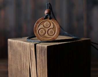 May include: A wooden pendant with a black cord, featuring three Chinese characters: "合" (He), "氣" (Qi), and "道" (Dao). The pendant is resting on a wooden block.