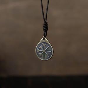 May include: A brass pendant necklace with a leather cord. The pendant features a stylized symbol with four points.
