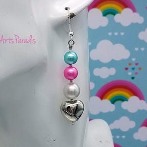 May include: A long earring with a teal, pink, and white bead design, finished with a silver heart charm. The earring hangs from a silver hook. The text "Arts Paradis" is visible in the background.