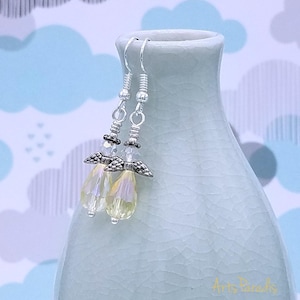 May include: A pair of dangle earrings with iridescent teardrop-shaped beads. The earrings feature silver-colored metal accents, including decorative wings and coiled wire details. The background is a light blue and white cloud pattern.