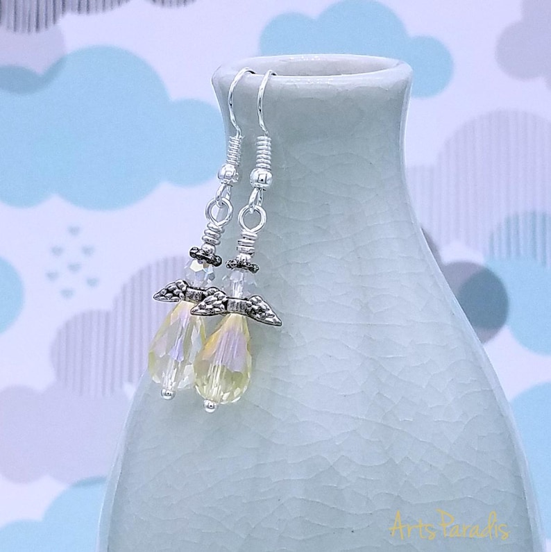May include: A pair of dangle earrings with iridescent teardrop-shaped beads. The earrings feature silver-colored metal accents, including decorative wings and coiled wire details. The background is a light blue and white cloud pattern.