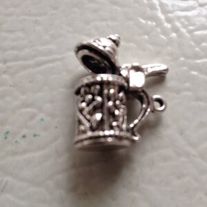 May include: Silver charm in the shape of a beer stein with a lid. The stein has a detailed design and a handle.