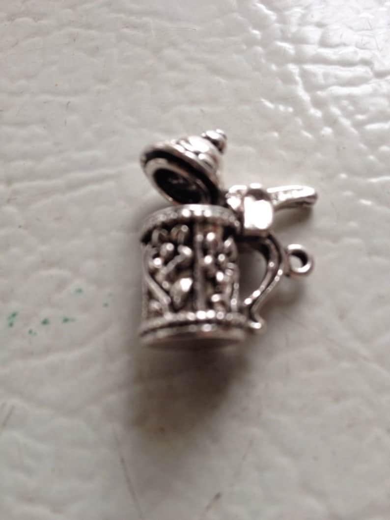 May include: Silver charm in the shape of a beer stein with a lid. The stein has a detailed design and a handle.