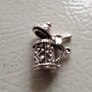 May include: Silver charm in the shape of a beer stein with a lid. The stein has an ornate design and a handle. The lid is open.