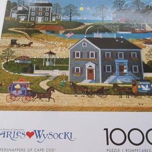 May include: A 1000-piece jigsaw puzzle featuring a colorful illustration of a coastal town with houses, horse-drawn carriages, and a gazebo. The puzzle is titled "The Whippersnappers of Cape Cod" by Charles Wysocki.