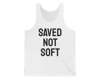 May include: White tank top with the text "SAVED NOT SOFT" in bold, black letters. The sleeveless shirt has a scoop neck and is made of a soft material.