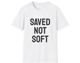 May include: White t-shirt with the text "SAVED NOT SOFT" in bold, black capital letters. The shirt has a crew neck and short sleeves. The text is centered on the front of the shirt.
