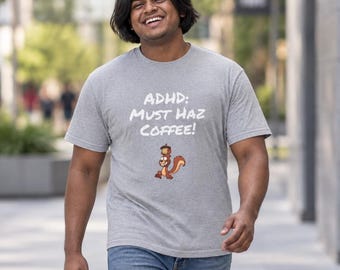 May include: A heather gray short-sleeve t-shirt featuring the white text "ADHD: MUST HAZ COFFEE!" above a small, cartoon-style brown squirrel illustration with an acorn balanced on its head, paired with blue denim jeans.