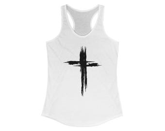 May include: White racerback tank top with a black cross design. The cross is made of thick brush strokes, creating a textured appearance. The tank top has a scoop neck and a racerback style.