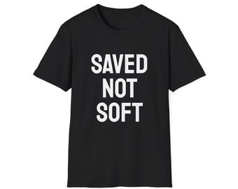 May include: Black t-shirt with the white text "SAVED NOT SOFT" in a bold, sans-serif font. The shirt has short sleeves and a crew neck. The text is centered on the front of the shirt.