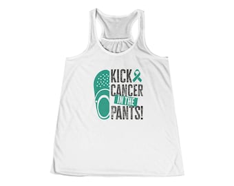 May include: A white racerback tank top featuring a teal graphic of a clog shoe and a teal awareness ribbon. The text reads KICK CANCER IN THE PANTS in a mix of teal and dark gray block lettering with a distressed, textured appearance.
