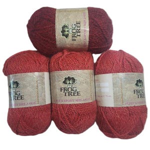 May include: A collection of red-toned yarn skeins. Each skein is labeled with "FROG TREE ALPACA SPORT MELANGE". The yarn is a deep red color, with a textured appearance. The labels feature a tree logo.