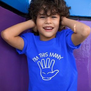 May include: A young boy wearing a blue t-shirt with the text "I'm this many" and a white outline of a hand with four fingers extended.