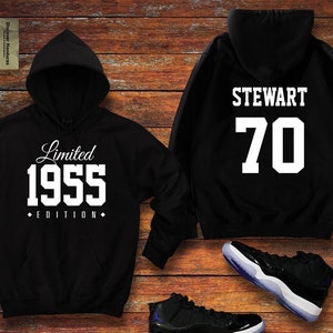 May include: Black hooded sweatshirt with white text "Limited 1955 Edition" on the front and "STEWART 70" on the back. A pair of black and white sneakers are also pictured.
